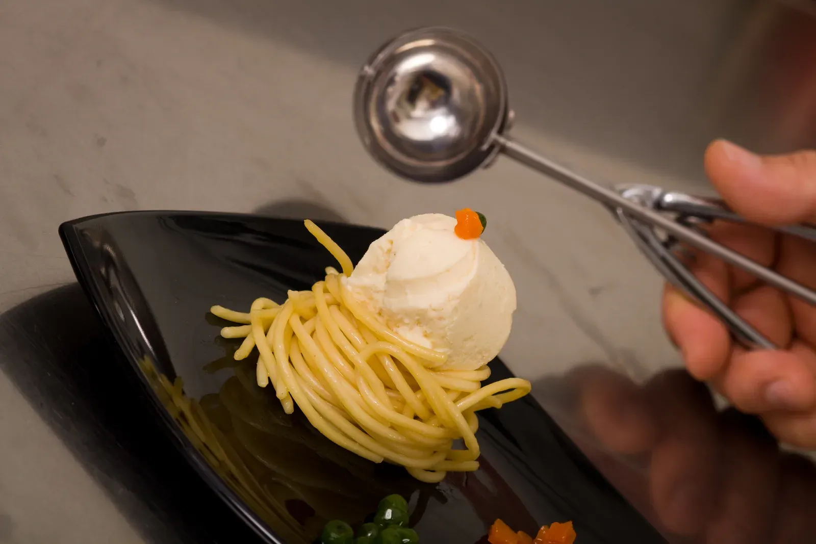Gelato gastronomico al tonno e cipolla servito con spaghetti su piatto nero.
